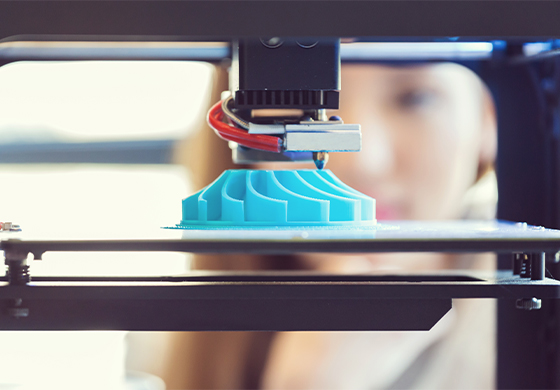 Women looking at a 3D printer as it prints a blue fan